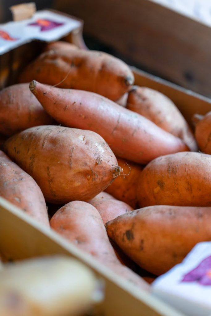 Close-up of fresh sweet potatoes stacked in a wooden crate at a market.